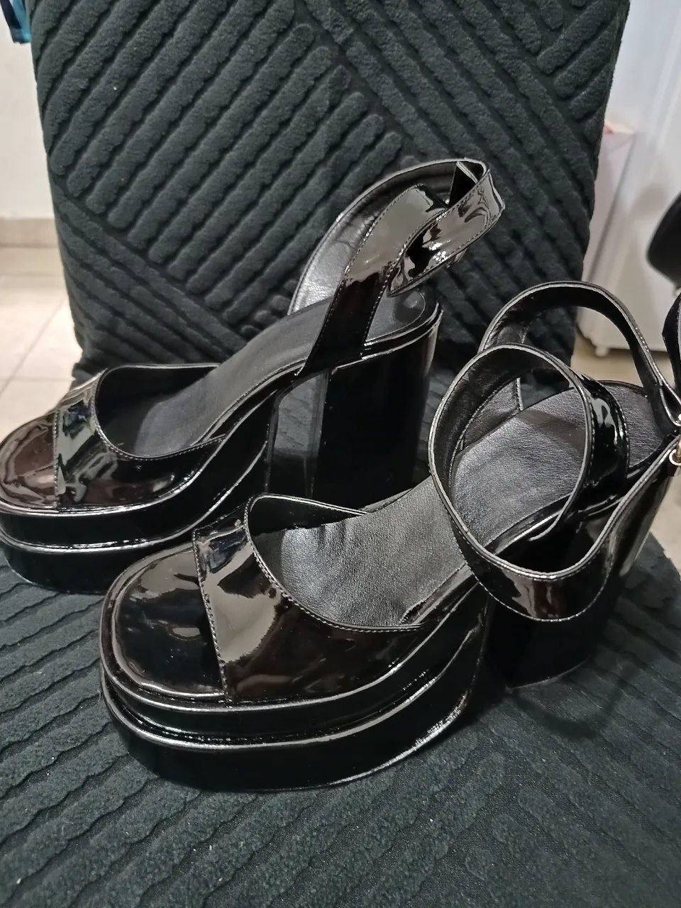 Sandalias negras de charol con plataforma y taco grueso. Tienen tiras que se ajustan al tobillo con hebilla.