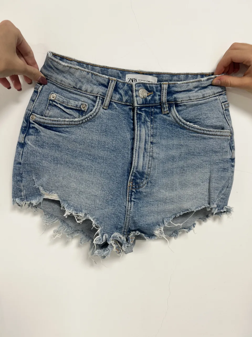 Short de jean Zara tiro alto con roturas y detalles deshilachados en el borde inferior. Posee bolsillos delanteros y traseros.