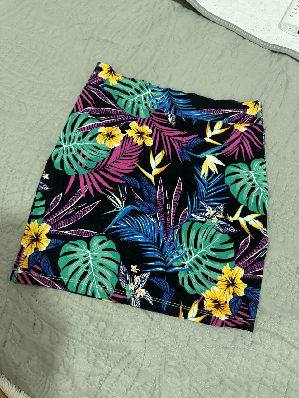 Pollera corta con estampa de hojas y flores tropicales en fondo negro.