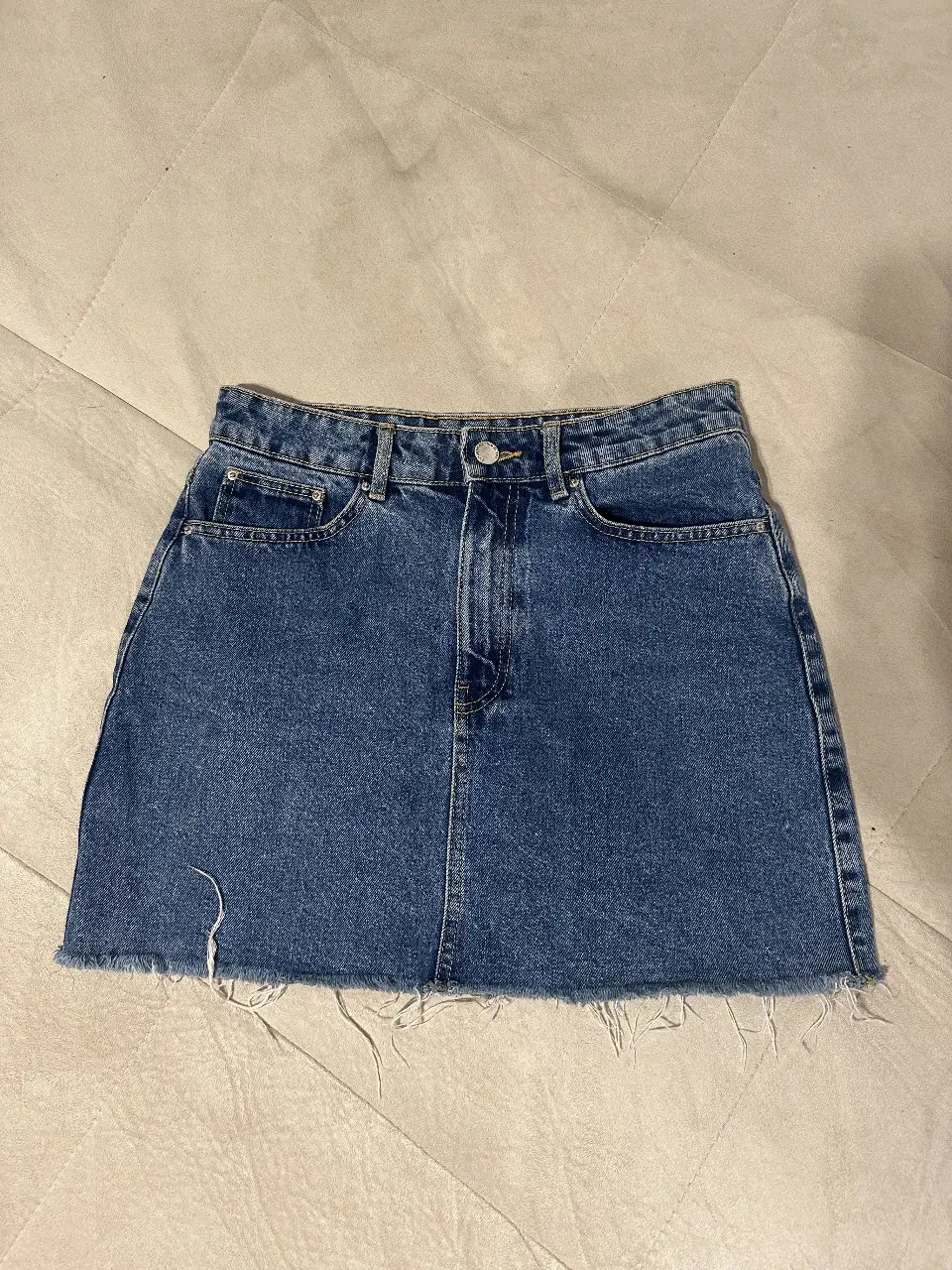 Minifalda de jean azul, con corte recto y detalle de flecos en el borde inferior. Ideal para un look casual y moderno.