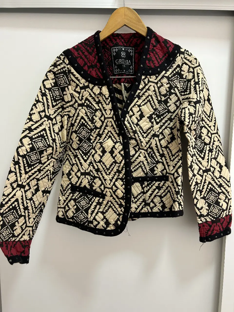 tapado/blazer cotuo con diseño geométrico en blanco y negro, detalles en rojo y negro en cuello y puños. Con tachas decorativas y etiqueta de la marca Grimia. Talle M.