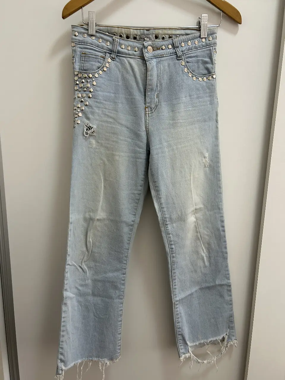 Jeans celeste con detalles de tachas plateadas en cintura y bolsillos traseros. Diseño con roturas y flecos en el bajo. Talle 40.