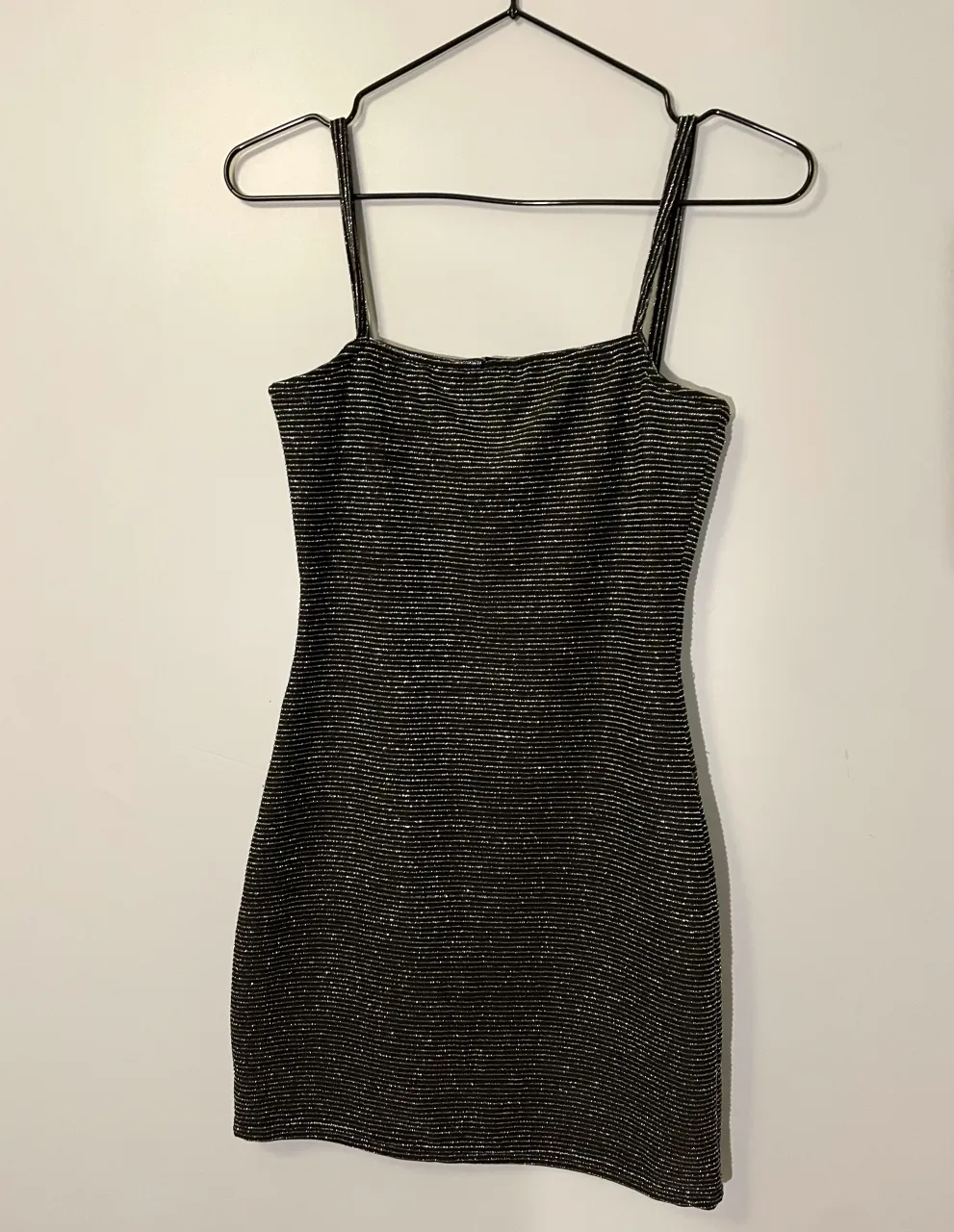 Vestido corto negro con brillos plateados, ideal para fiestas o salidas nocturnas. Diseño ajustado con tirantes finos, perfecto para lucir tu figura.