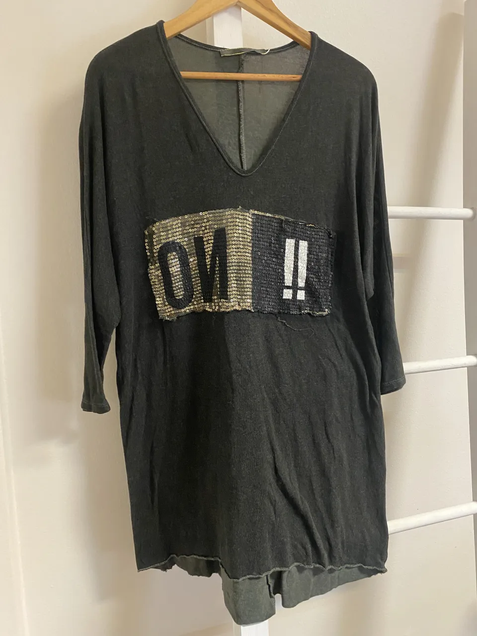 Remera gris oscuro con escote en V y mangas 3/4. Posee un aplique frontal con lentejuelas doradas y negras que forman la palabra "OW!!".