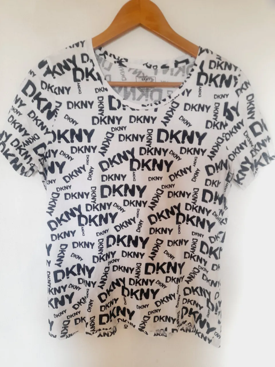 Remera DKNY blanca con estampado de la marca en negro. De algodón 100%, manga corta y cuello redondo. ¡Un básico con onda para todos los días!   Largo adelante:62cm.   Largo atrás:66cm.    Axila a axila:50cm.