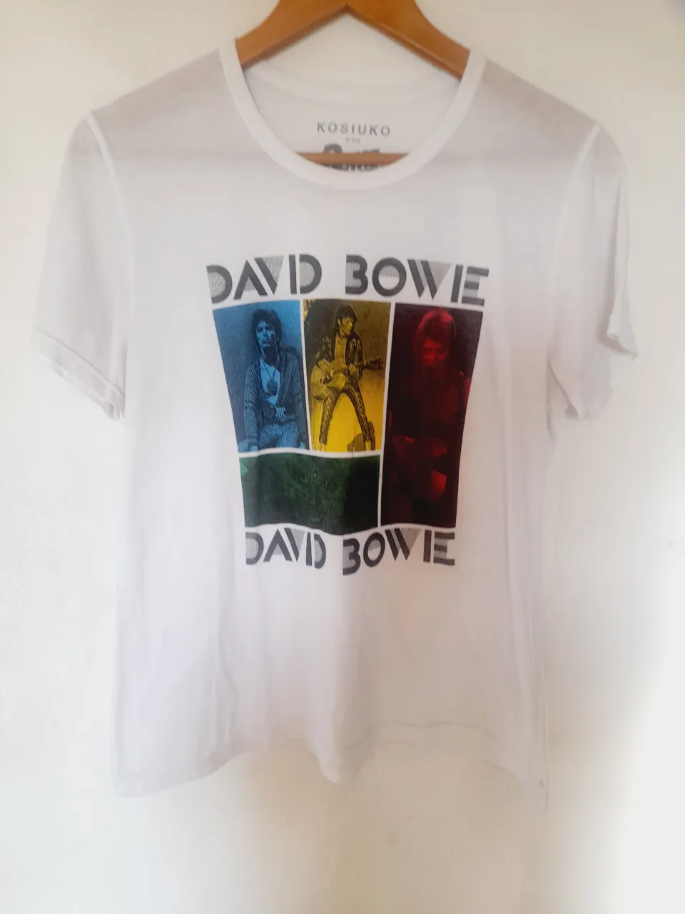 Remera blanca de manga corta con estampa de David Bowie. La estampa incluye cuatro imágenes del artista y el texto "DAVID BOWIE" repetido dos veces.