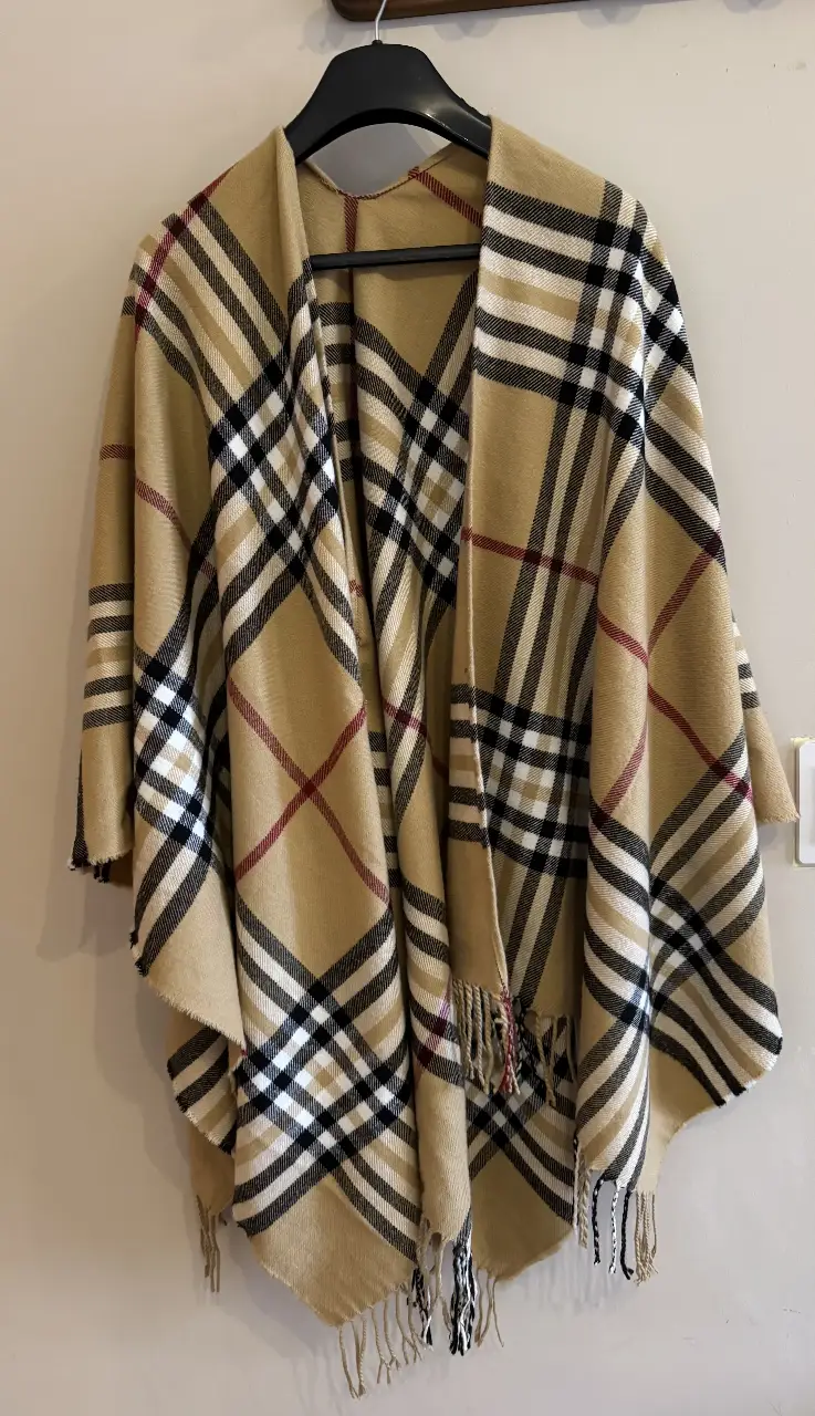 Poncho/ruana  con estampado a cuadros en tonos beige, negro y rojo. Ideal para el invierno, este poncho ofrece abrigo y estilo. Perfecto para un look casual y cómodo.