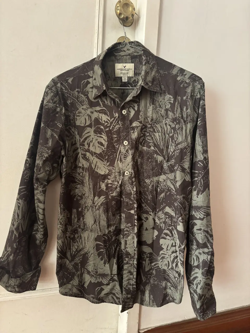 Camisa de hombre American Eagle con estampado de hojas en tonos grises y verdes. Talle S, corte clásico y tela suave. Ideal para un look casual y fresco.