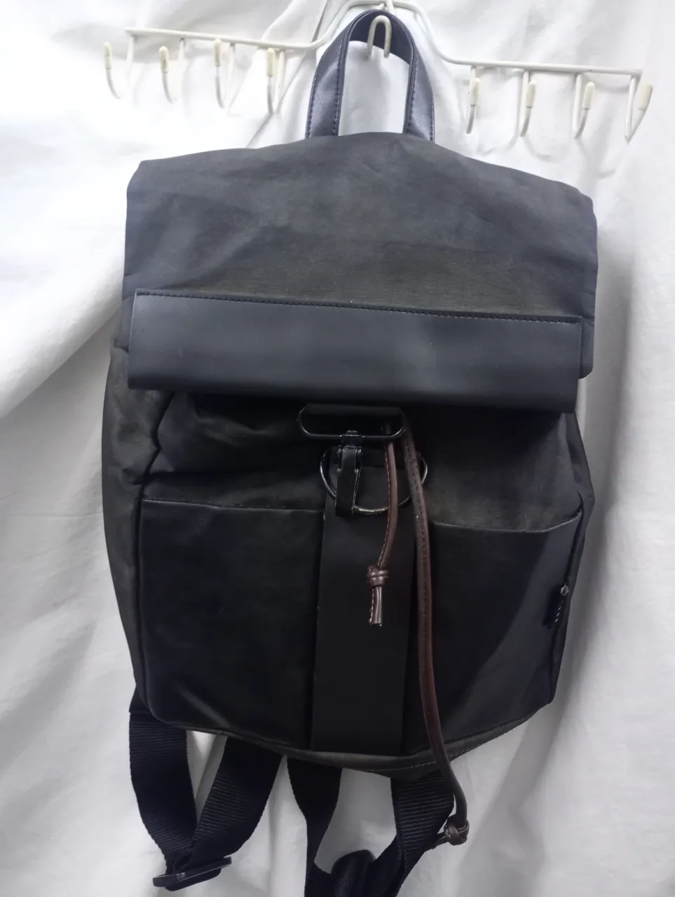 Mochila de lona con detalles en cuero sintético. Cierre principal con solapa y cordón. Bolsillos frontales y correas ajustables.