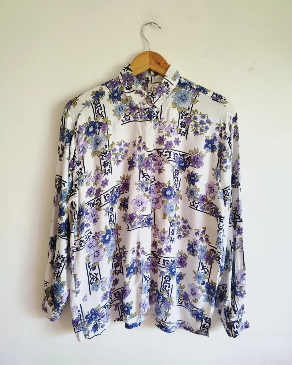 Camisa blanca con estampado floral en tonos azules y violetas. Posee cuello camisero y mangas largas.