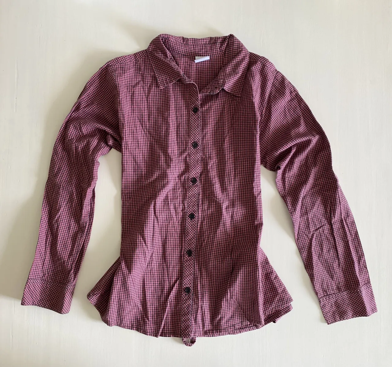 Camisa a cuadros de manga larga con botones al frente y detalle de lazo en la cintura. Cuello camisero y puños con botones.