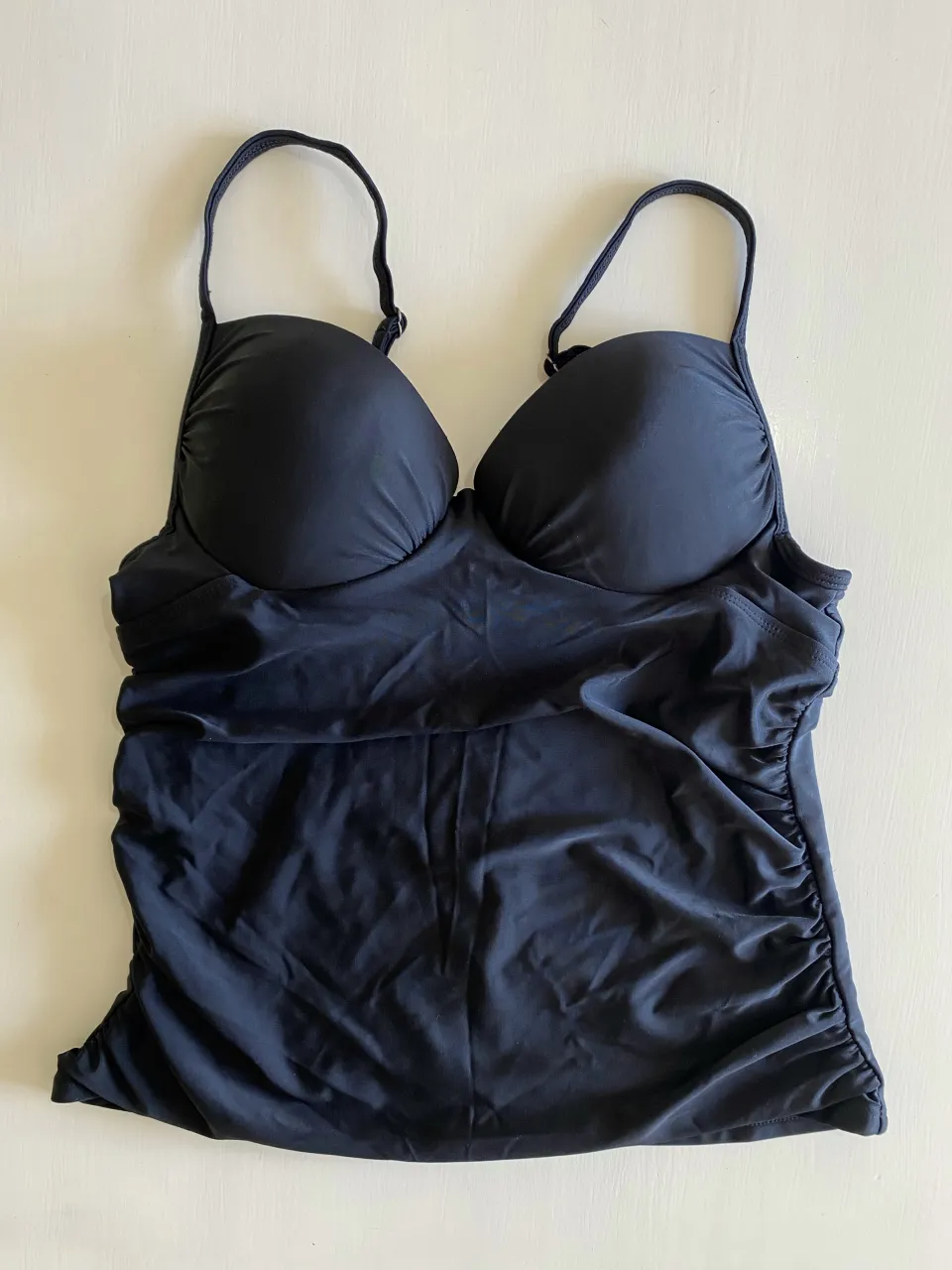 Remera de traje de baño negra, con corpiño armado y tiras regulables. Posee fruncido en los laterales de la cintura.