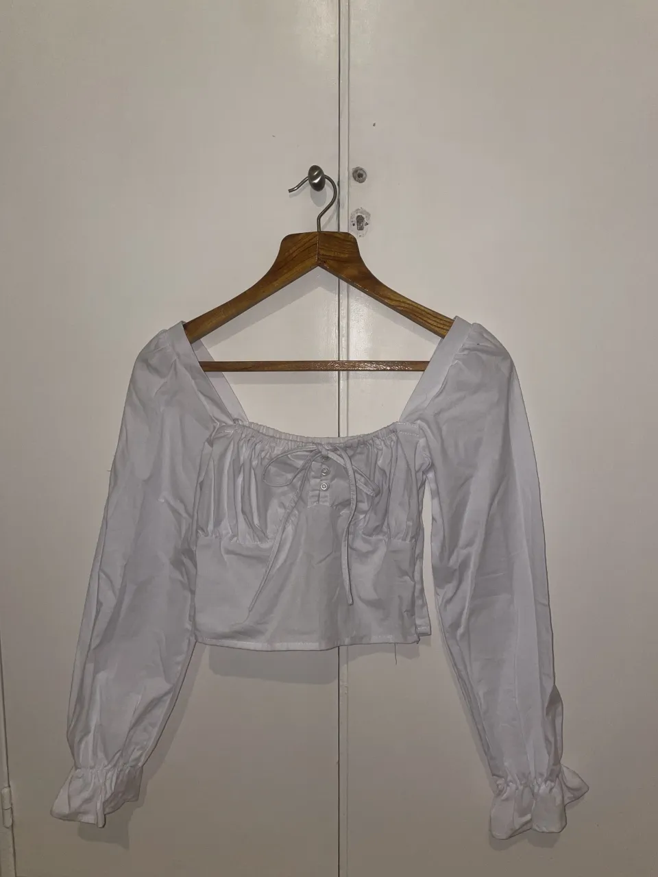 Blusa blanca escote cuadrado con lazo y botones al frente. Mangas largas con puños fruncidos.