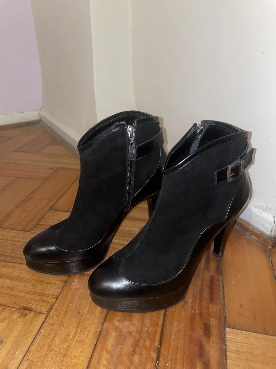 Botitas de cuero y gamuza negras, con taco alto y plataforma. Tienen cierre lateral y una hebilla decorativa en el lateral externo.