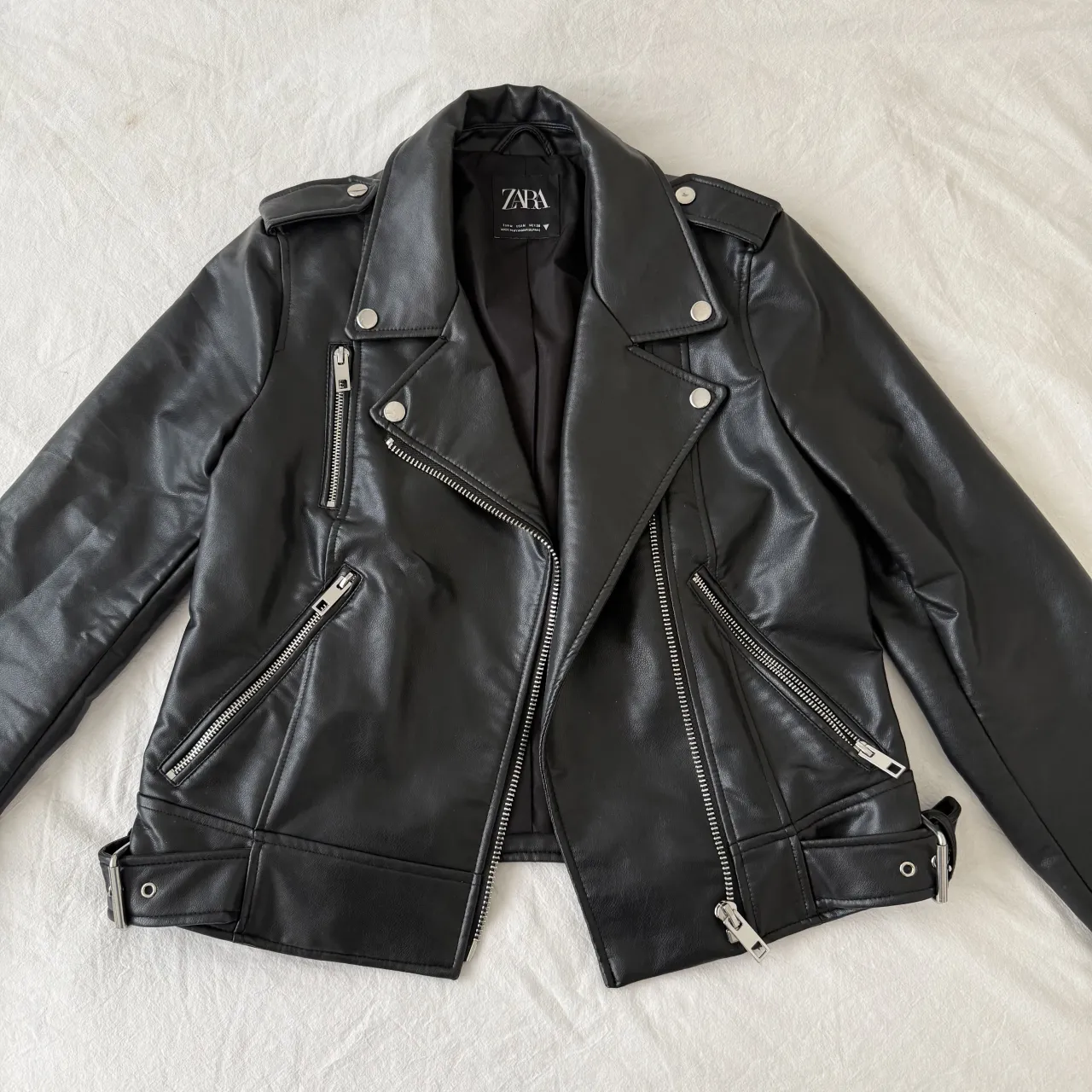 Campera de cuero sintético negra con solapas, cierre al frente y bolsillos con cierre. Tiene hebillas en la cintura.