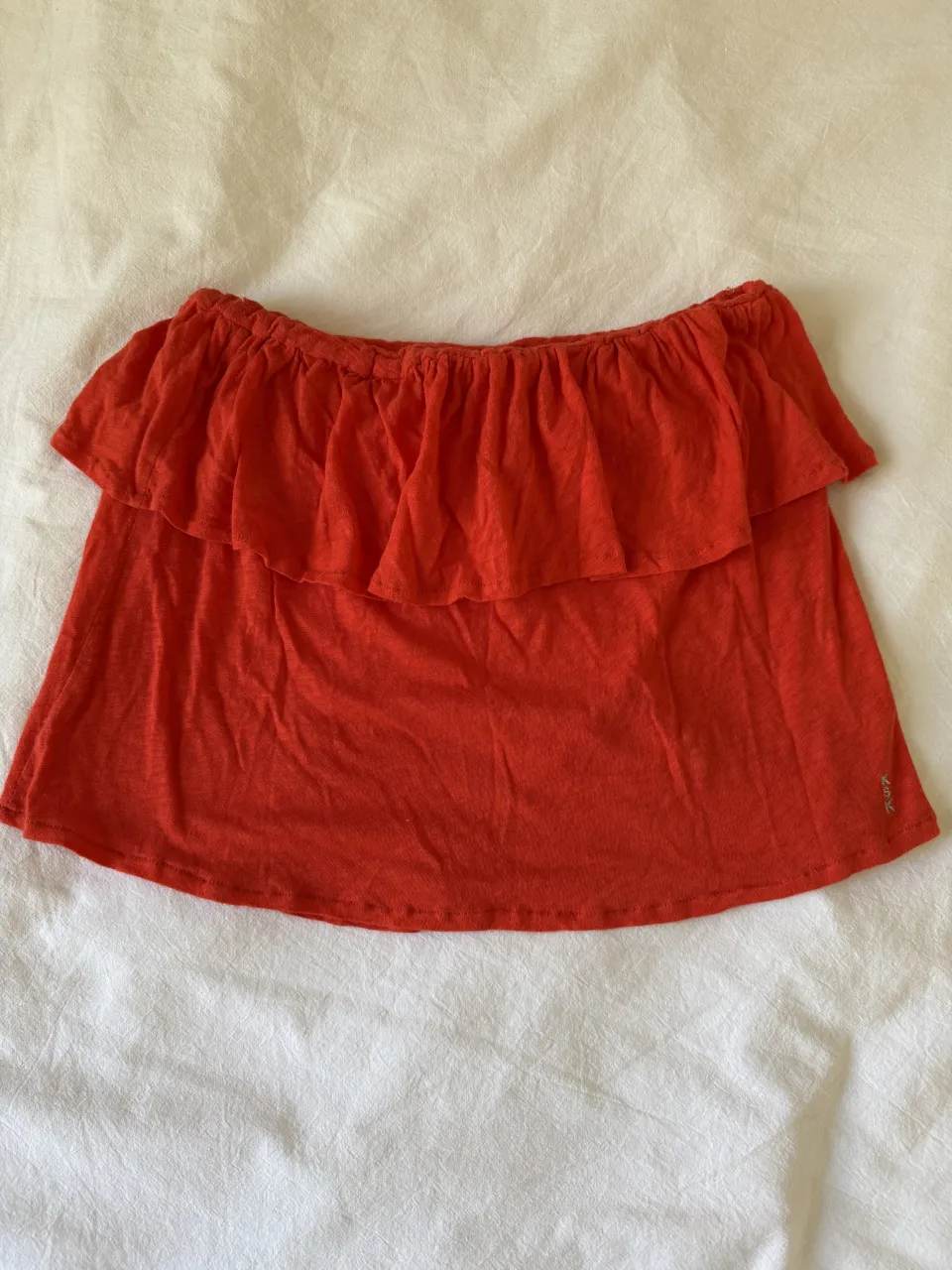 Remera naranja con volado en el escote. Escote strapless con elástico.