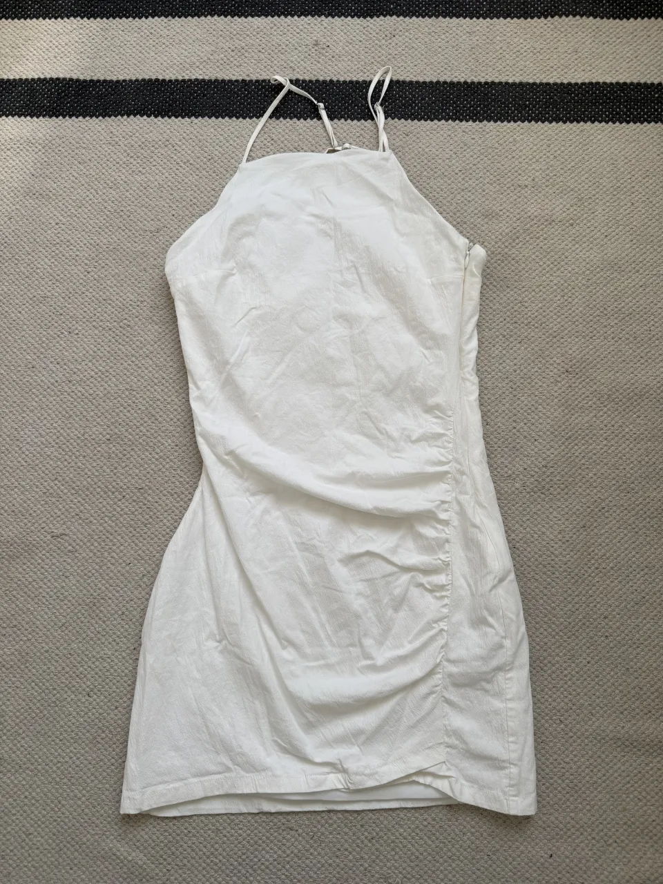 Vestido blanco corto con tiras finas y detalle de fruncido en un lateral.