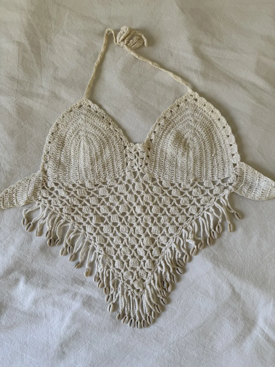 Top de crochet color crudo con detalles de caracoles en el borde inferior. Posee tiras para atar en cuello y espalda.