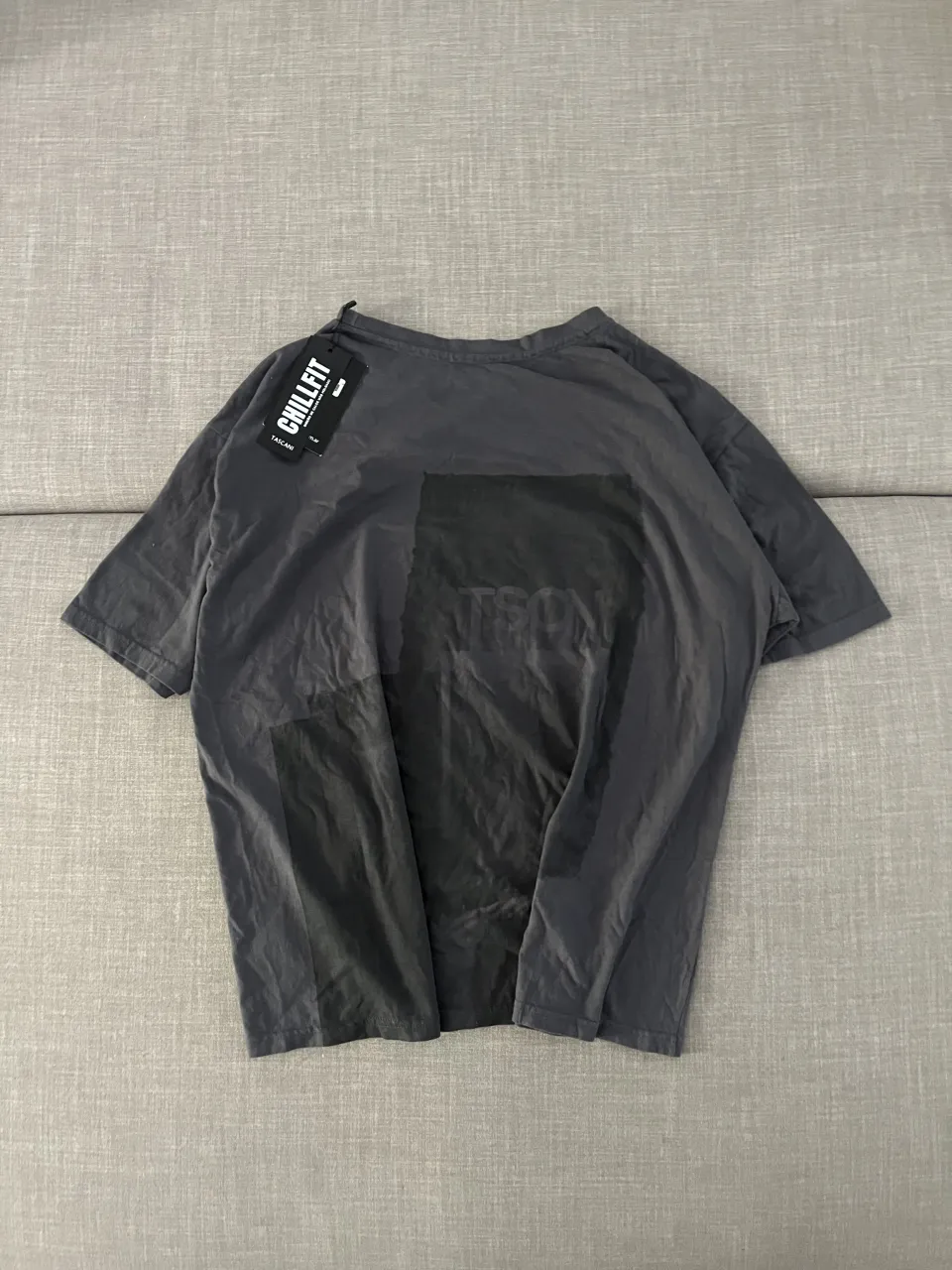 Remera gris oscuro con estampa abstracta en negro en el frente. Posee una etiqueta de marca visible. Talle L pero overzide, bastante grande.