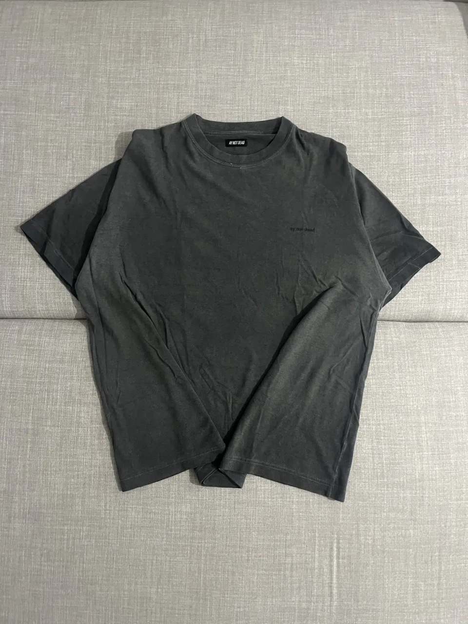 Remera gris oscuro con cuello redondo y mangas cortas. Presenta un pequeño logo bordado en el frente.