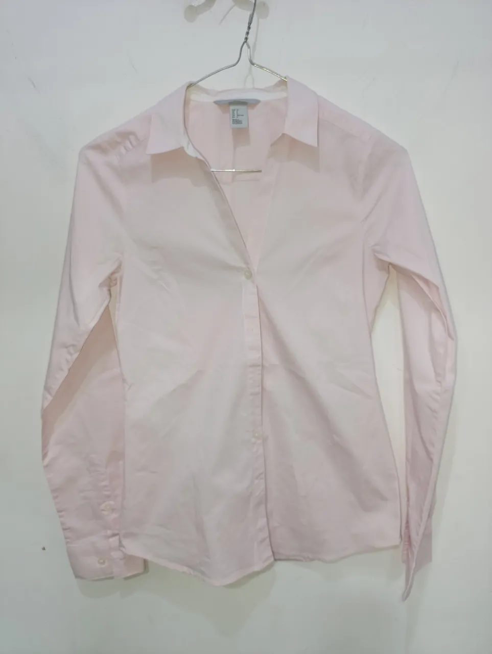 Camisa rosa de manga larga, elastizada, con finas rayas blancas y pequeños puntos blancos. Cuello camisero y botones al frente.