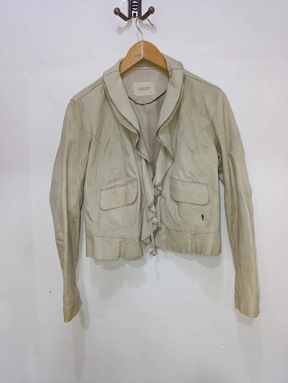 Campera de cuero de oveja, CARDON color crudo con volados en el frente. Posee dos bolsillos con tapa en la parte delantera y cierre en la parte inferior. Cuello con solapa y detalle de volados.