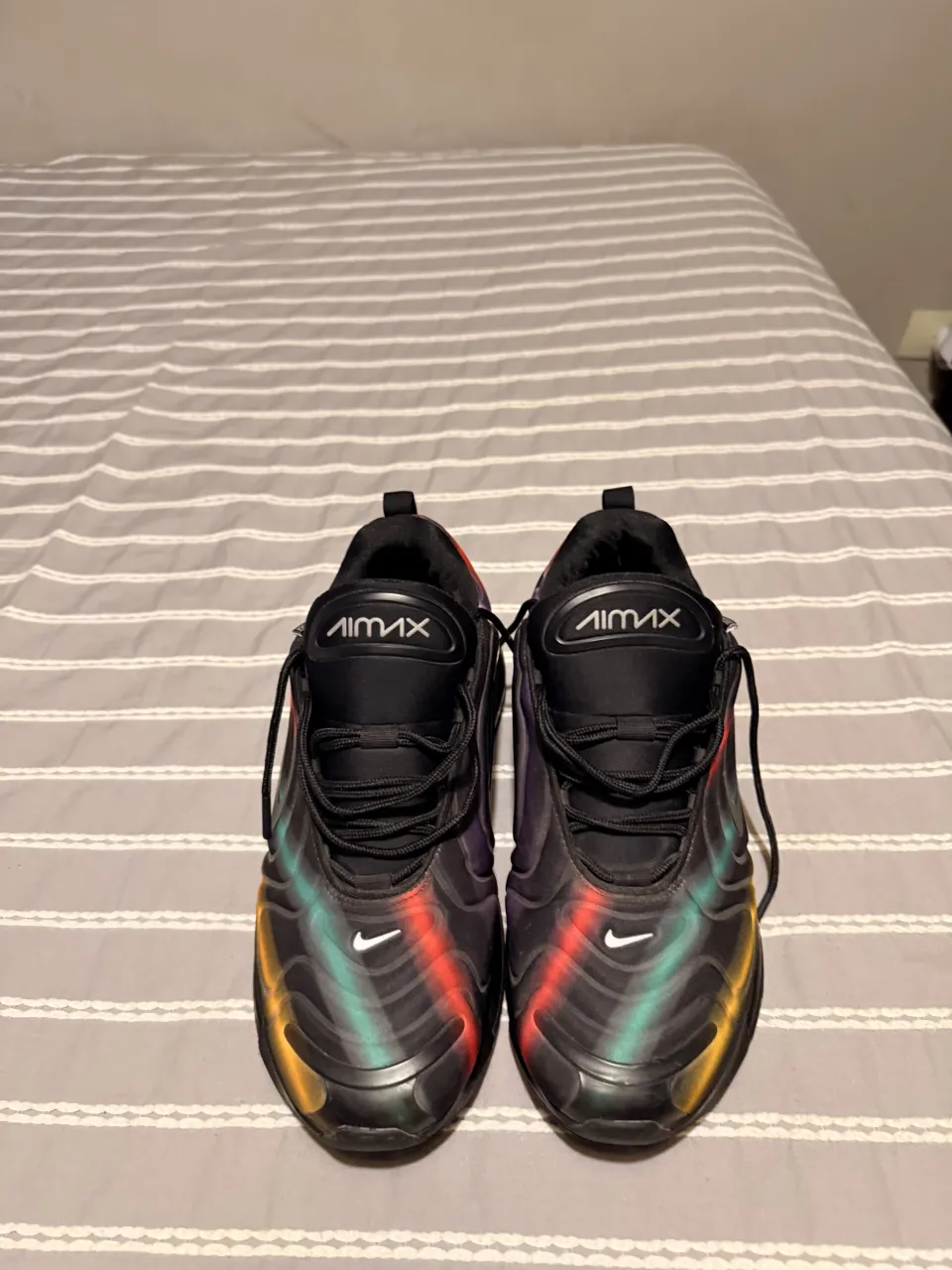 Zapatillas deportivas negras con detalles de líneas multicolores en degradé (amarillo, verde, rojo, violeta) y logo blanco de la marca en los laterales. Etiqueta interior con información del producto.