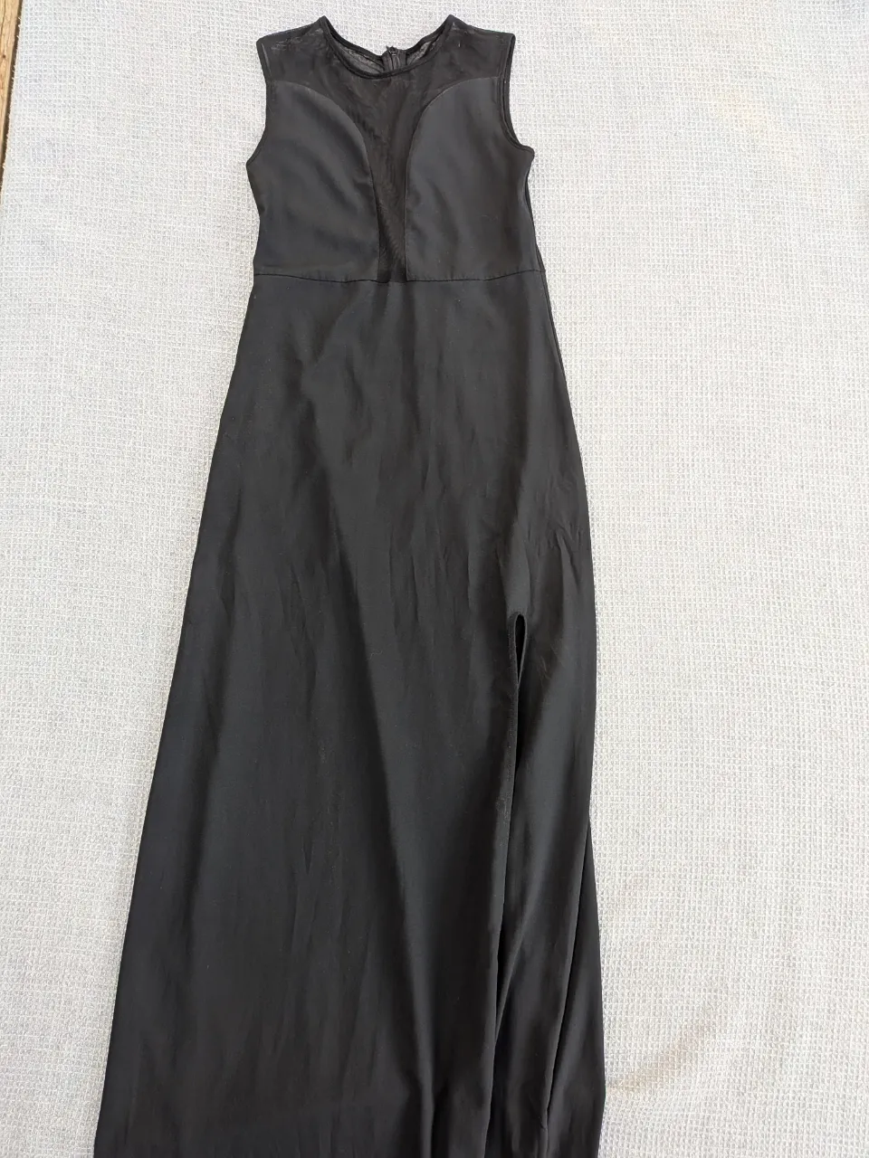 Vestido largo negro, sin mangas, con detalles de tela de red en el escote y la espalda. Posee una abertura lateral en la falda.