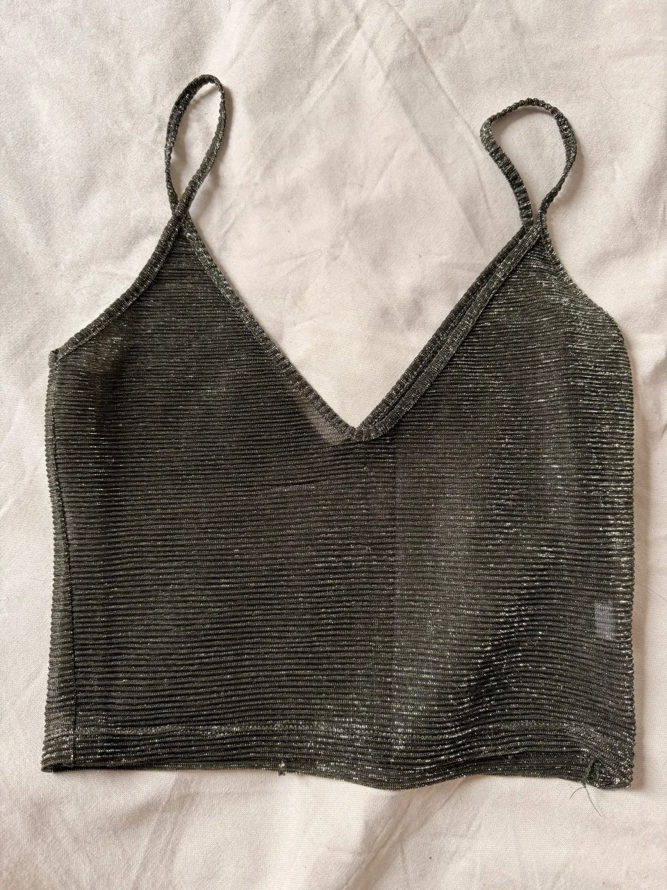 Top corto transparente con breteles finos y escote en V. Posee un tejido con hilos plateados que le dan un brillo sutil.
