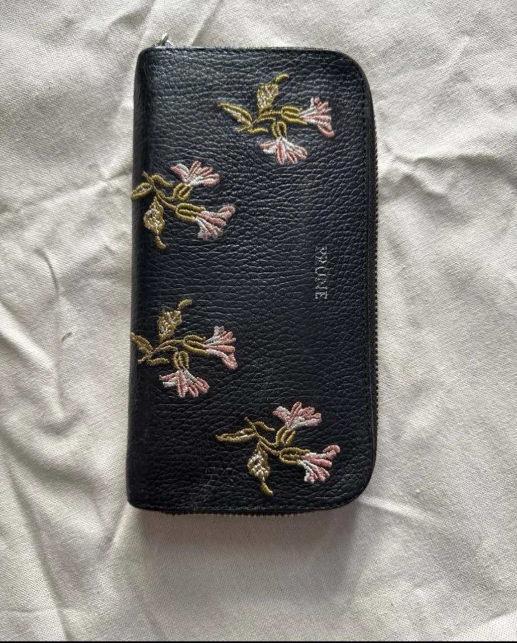 Billetera negra con cierre y bordado de flores en tonos rosa y verde de PRUNE. Posee múltiples compartimentos internos. 
medidas
ancho 10cm
largo 19cm