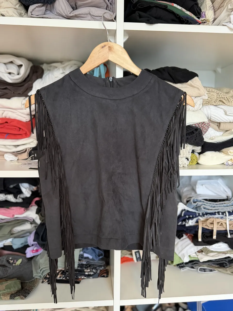 Remera negra sin mangas con cuello redondo y detalles de flecos en los hombros y en el bajo. Cierre en la espalda.