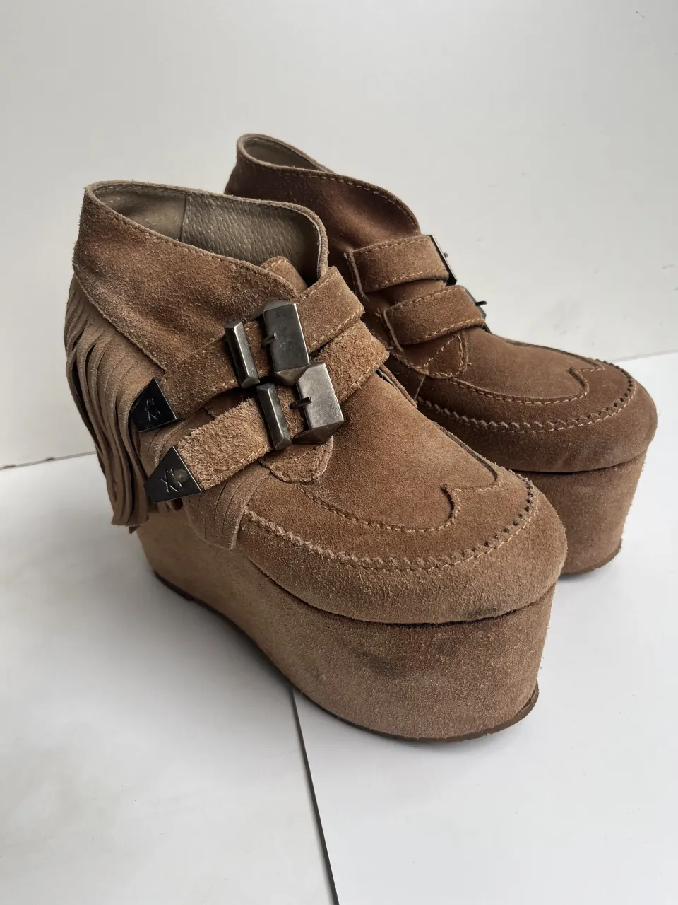 Botas de gamuza color marrón con flecos y hebillas metálicas. Tienen plataforma.