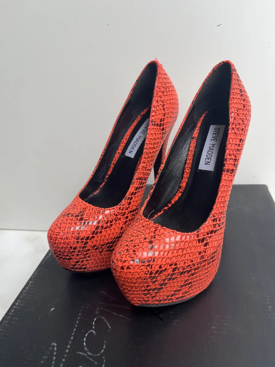 Zapatos de taco alto color naranja con estampado de serpiente en negro. Tienen plataforma delantera y la marca Steve Madden en la plantilla.