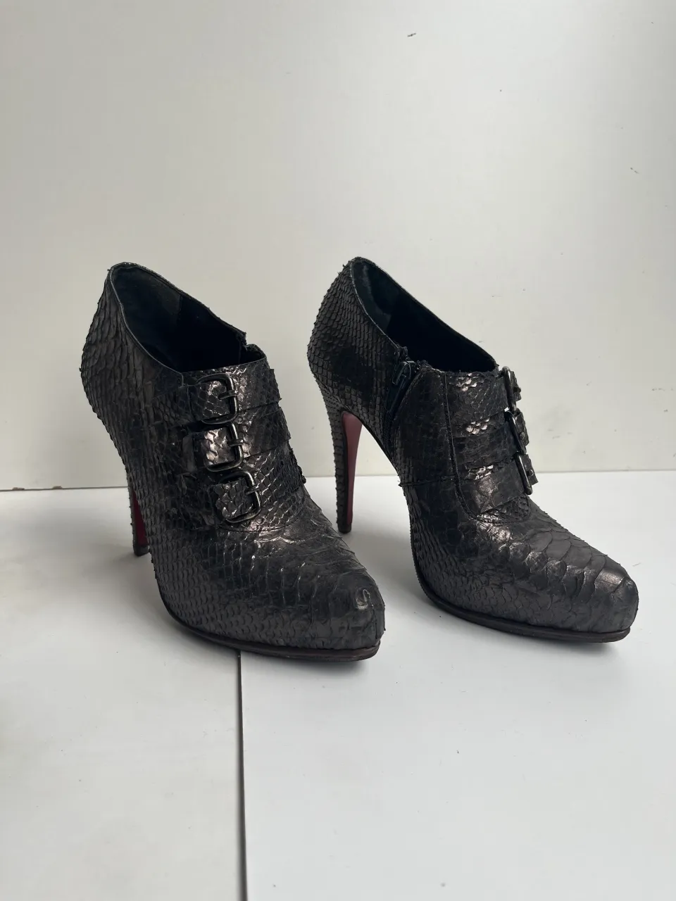 Botas de taco alto con textura de escamas, color negro. Tienen tres hebillas metálicas en el frente y cierre lateral.