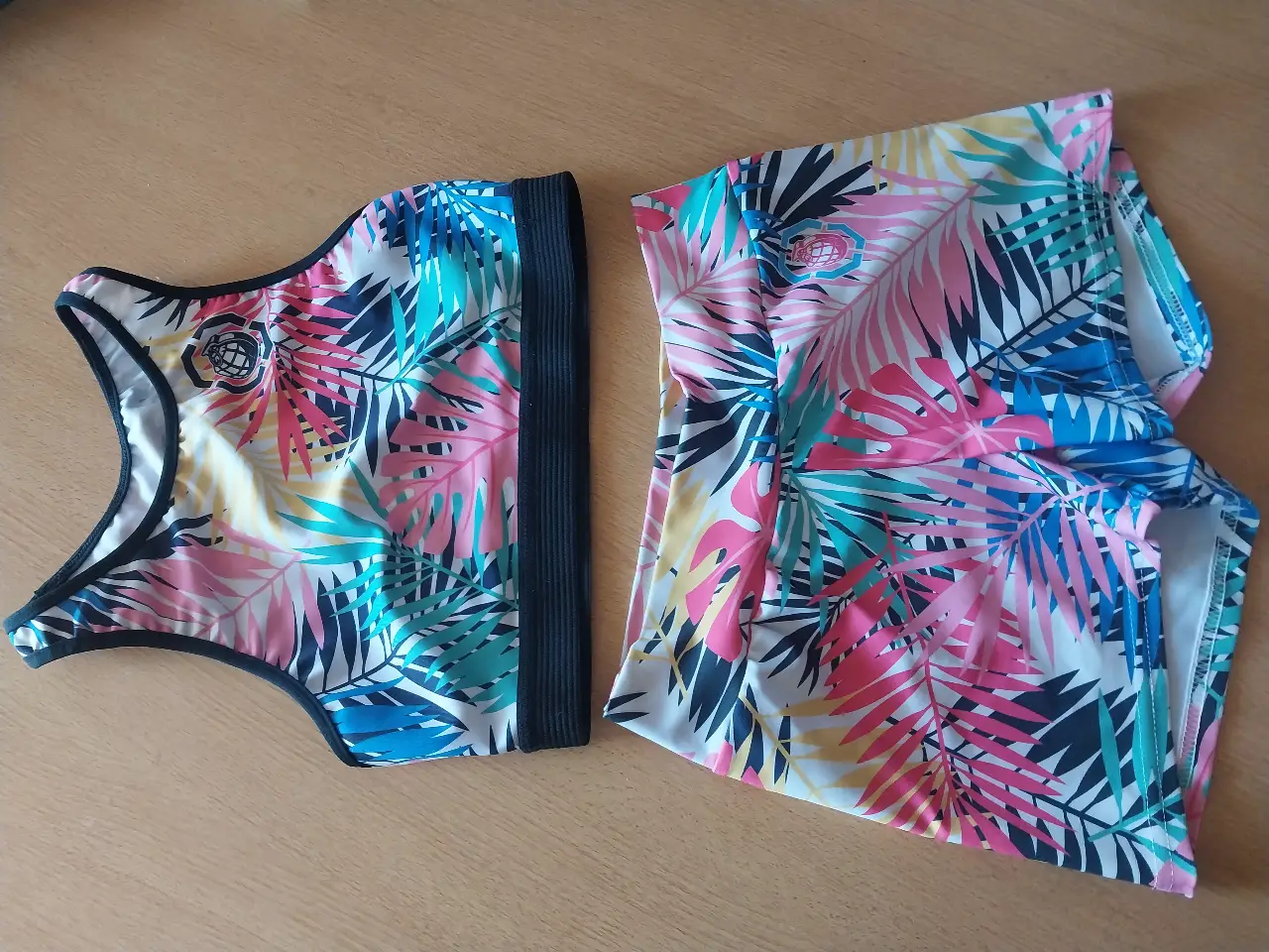 Conjunto deportivo de mujer, estampado con hojas tropicales en tonos rosa, azul y amarillo. Incluye un top deportivo y un short a juego. Ideal para actividades físicas y lucir un estilo vibrante y moderno.