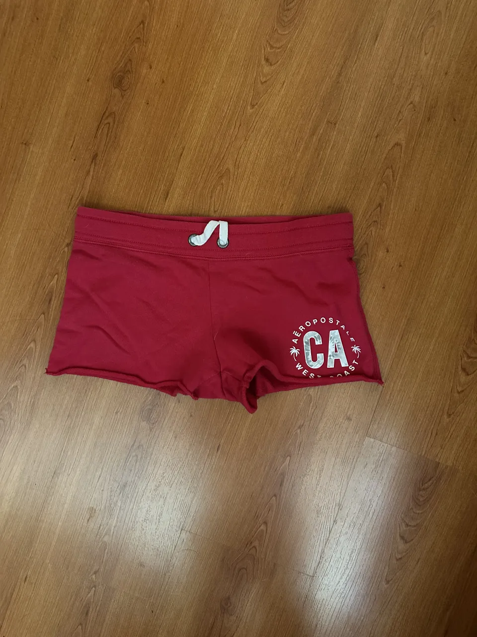 Shorts de color rojo con cordón blanco en la cintura y estampa blanca en la parte inferior derecha.