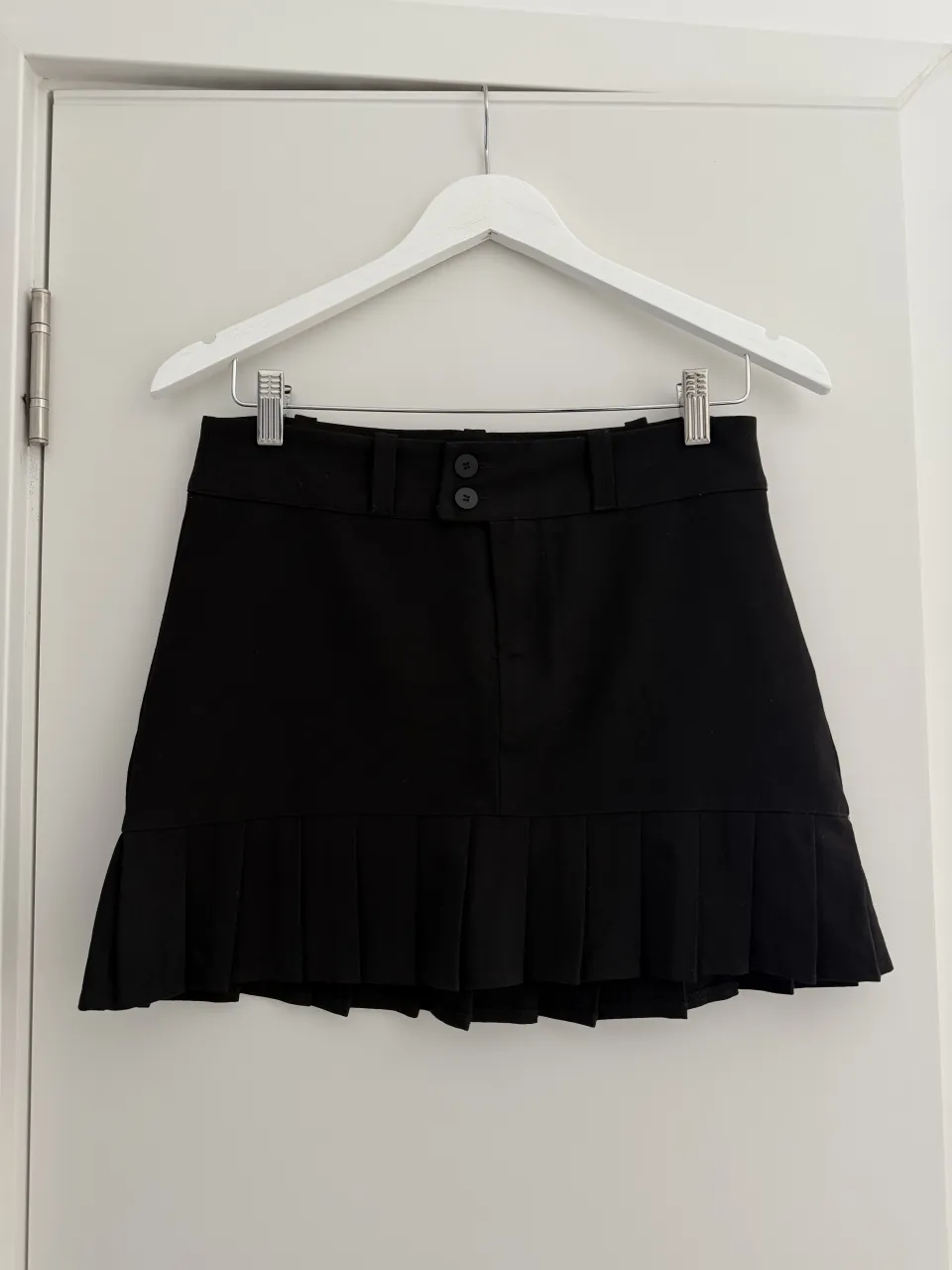 Pollera tiro bajo negra corta con detalle de tablas en el ruedo y dos botones en la cintura. NUEVA SIN USO