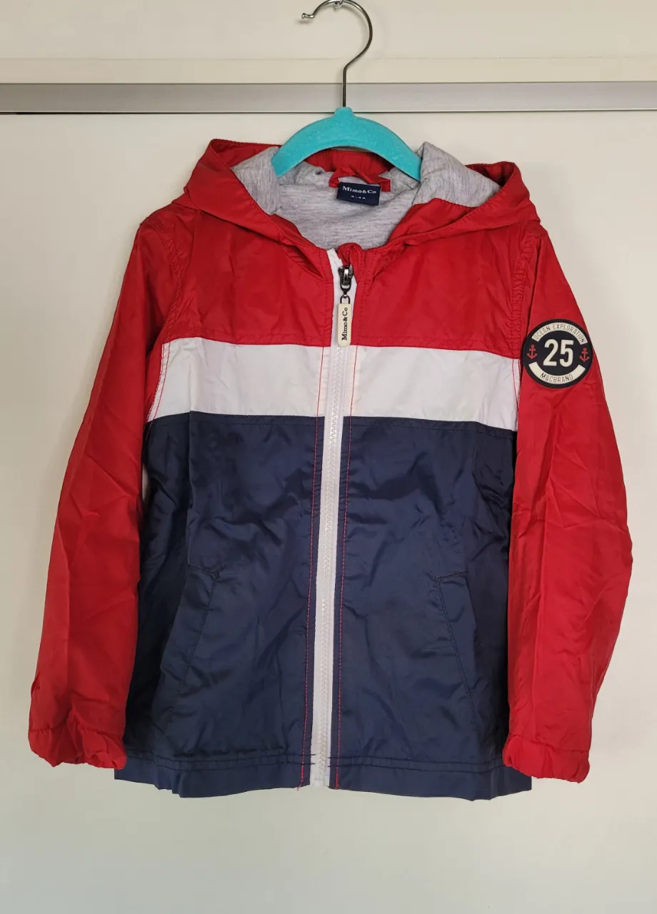 Campera con capucha, cierre al frente y parches decorativos en la manga. Diseño tricolor en rojo, blanco y azul marino.