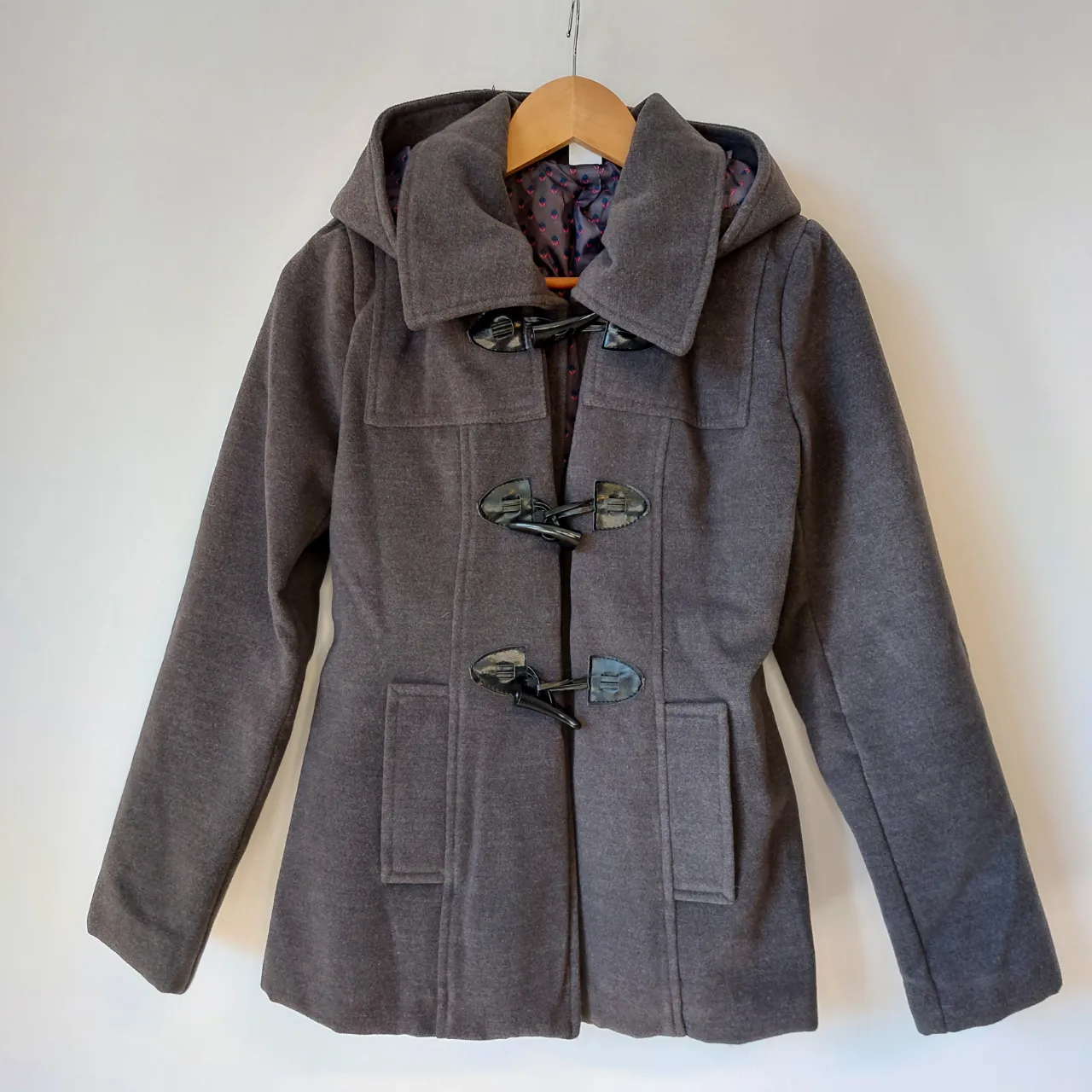 Montgomery de paño gris con capucha, cierre de broches y cuello alto. Capucha desmontable. Posee bolsillos frontales y forro interior estampado