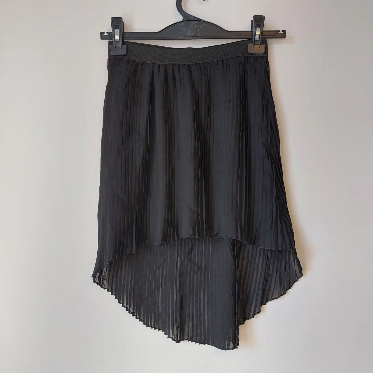 Pollera negra plisada con elástico en la cintura. Posee un diseño asimétrico con el ruedo más corto adelante y más largo atrás.