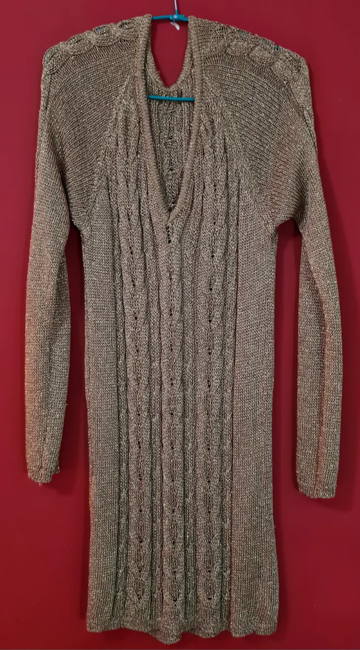 Vestido tejido largo, color dorado con hilos metalizados. Posee un escote en V pronunciado y detalles de trenzas en el frente. Ideal para un look elegante y sofisticado.