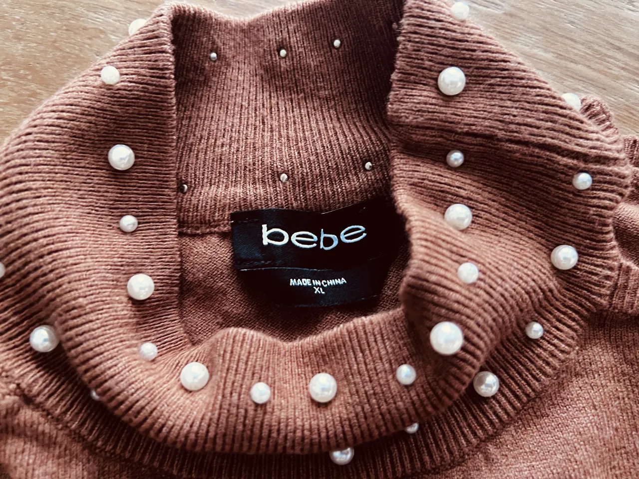 Sweater marrón de cuello alto con detalles de perlas y strass en el cuello y en el frente con el logo de la marca.