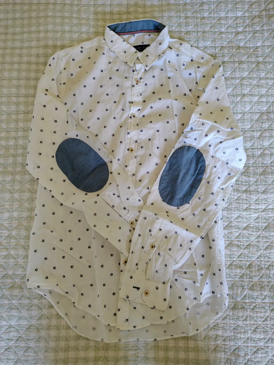 Camisa blanca de manga larga con estampa de puntos negros y parches de tela denim en los codos. Cuello camisero y botones al frente.