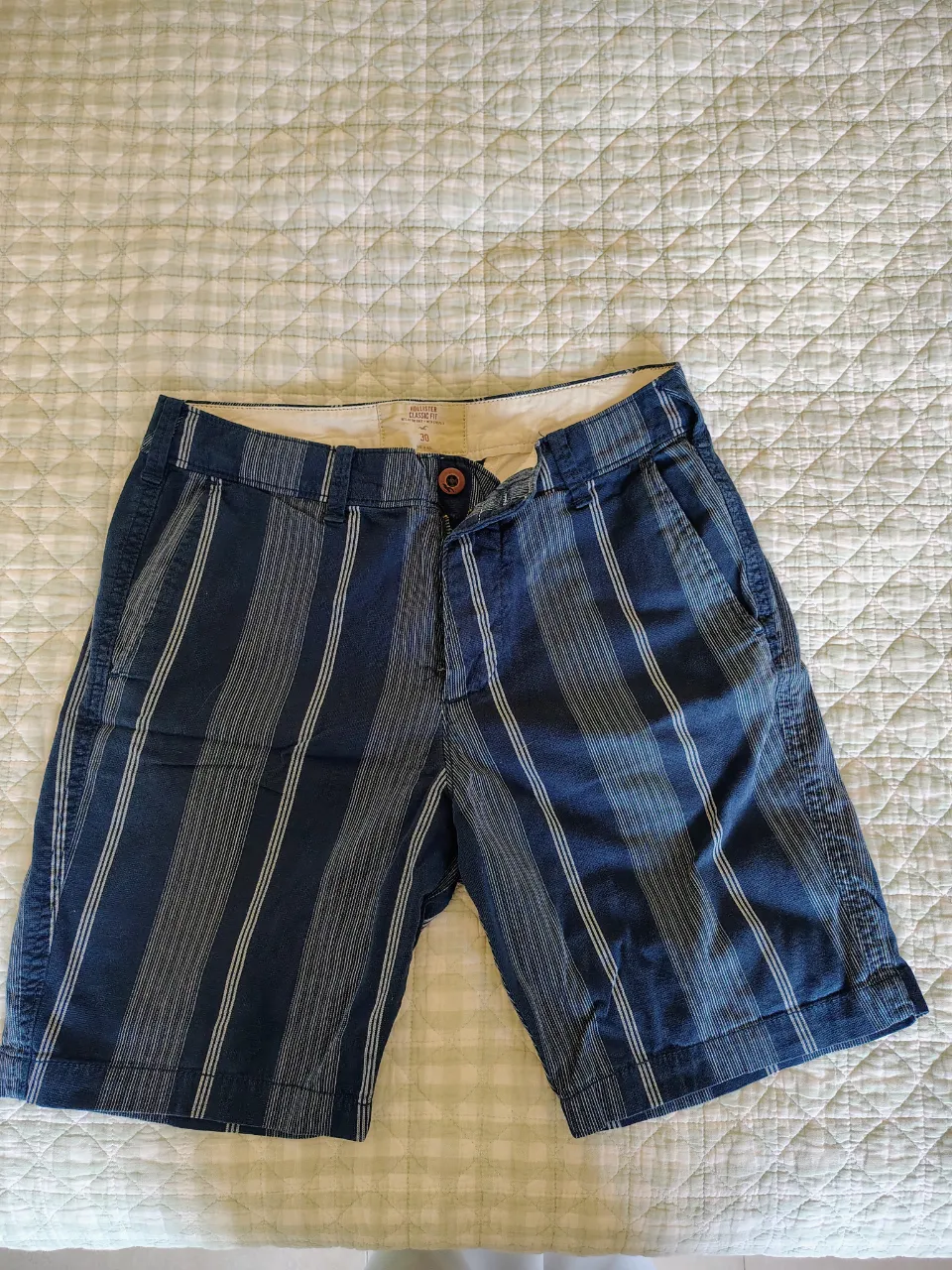 Shorts de gabardina con rayas verticales en tonos de azul y blanco. Tienen bolsillos laterales y un cierre con botón.