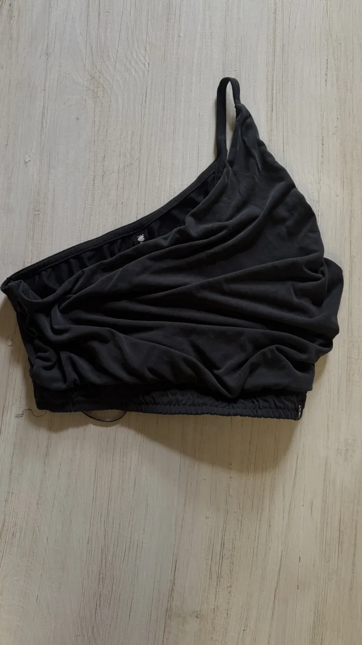 Top negro de un solo hombro con fruncido y elástico en la base.