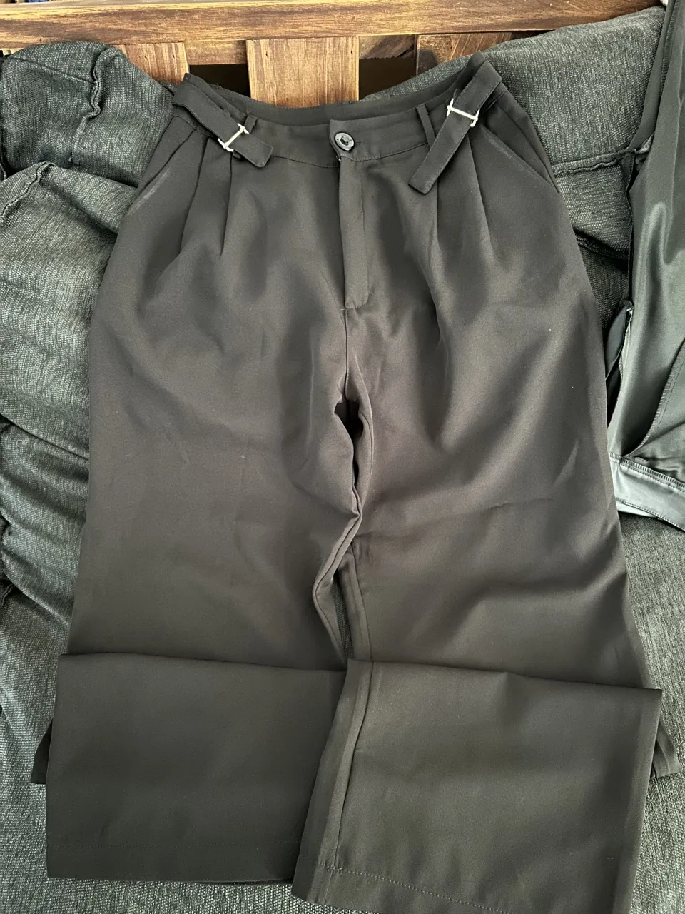 Pantalón negro de vestir, tiro alto, con pinzas y detalles de hebillas en la cintura. Corte ancho y moderno, ideal para un look elegante y sofisticado.