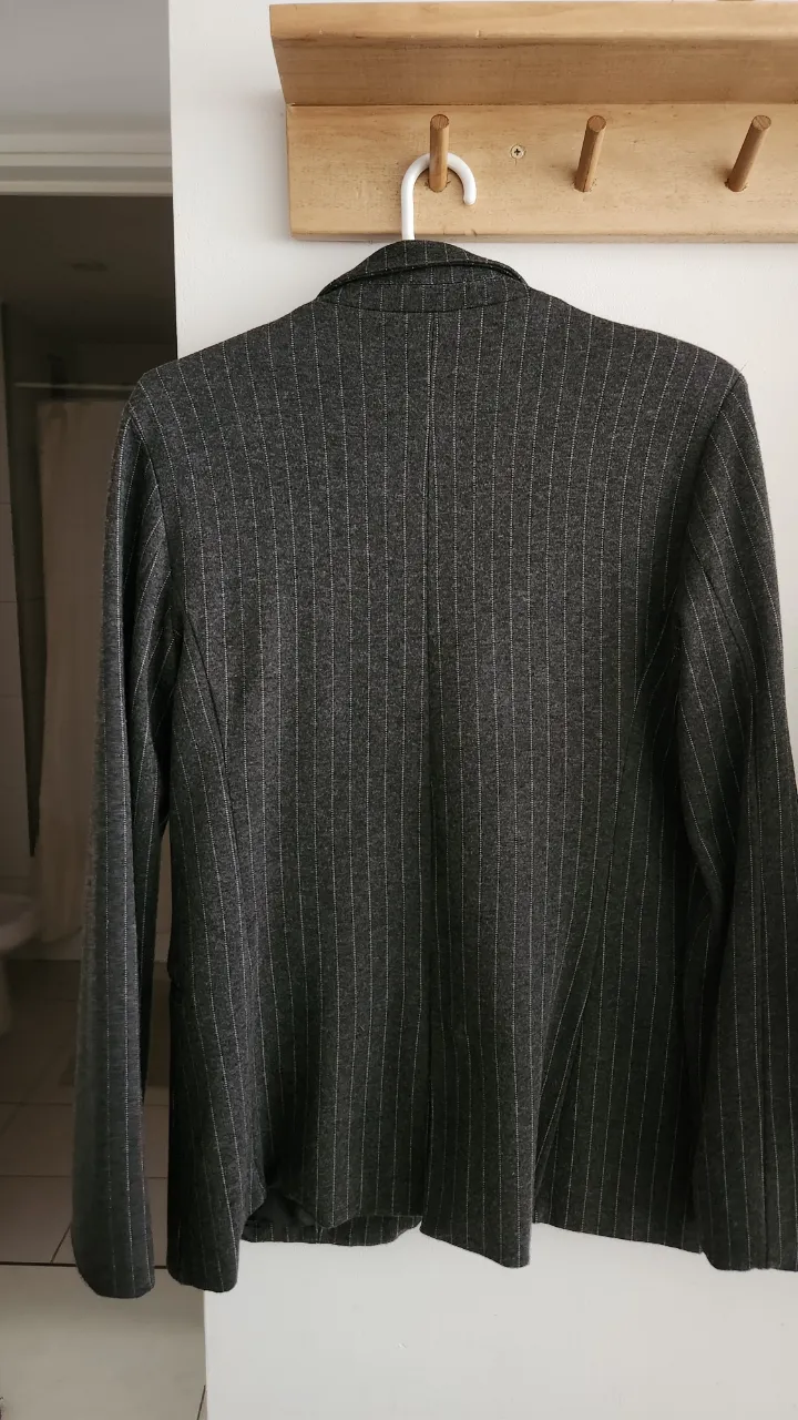 Blazer gris con rayas verticales blancas y un botón al frente.
