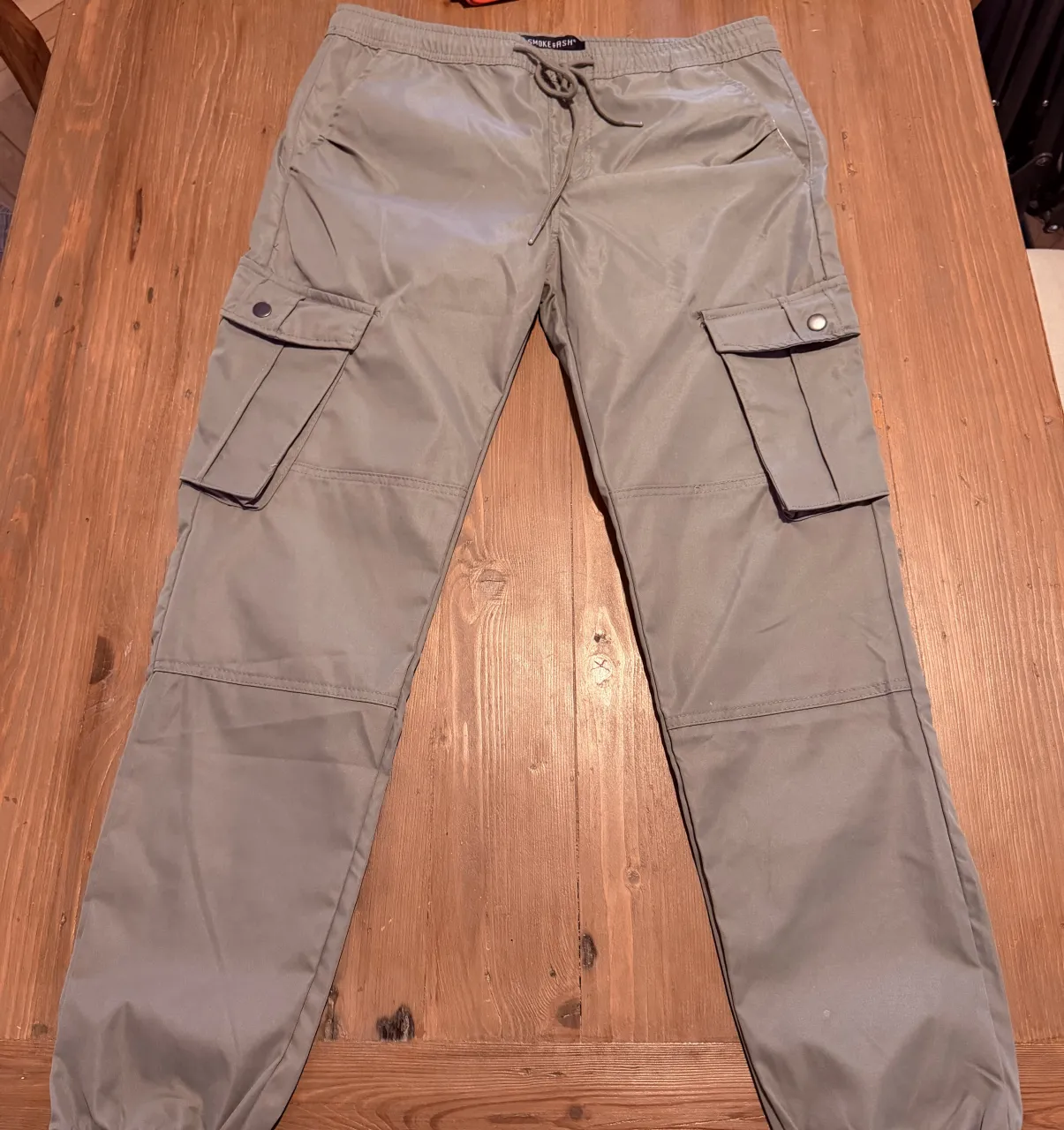 Pantalón cargo de color gris con cordón en la cintura y bolsillos laterales y traseros.