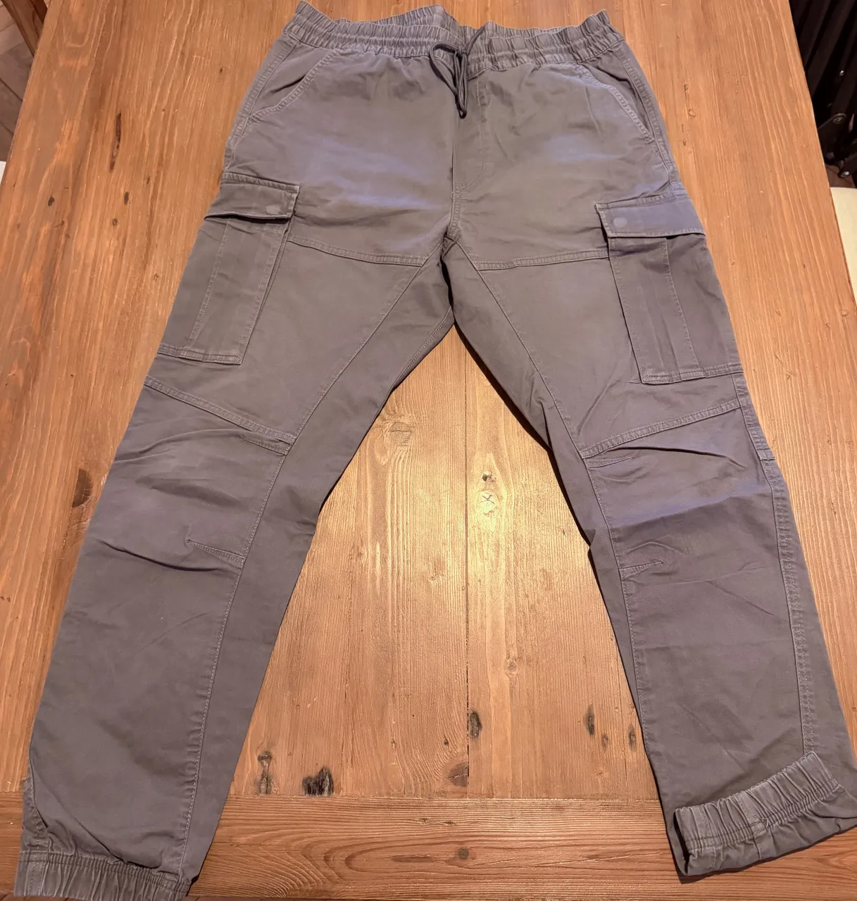 Pantalón cargo de color gris con cordón en la cintura y bolsillos laterales.