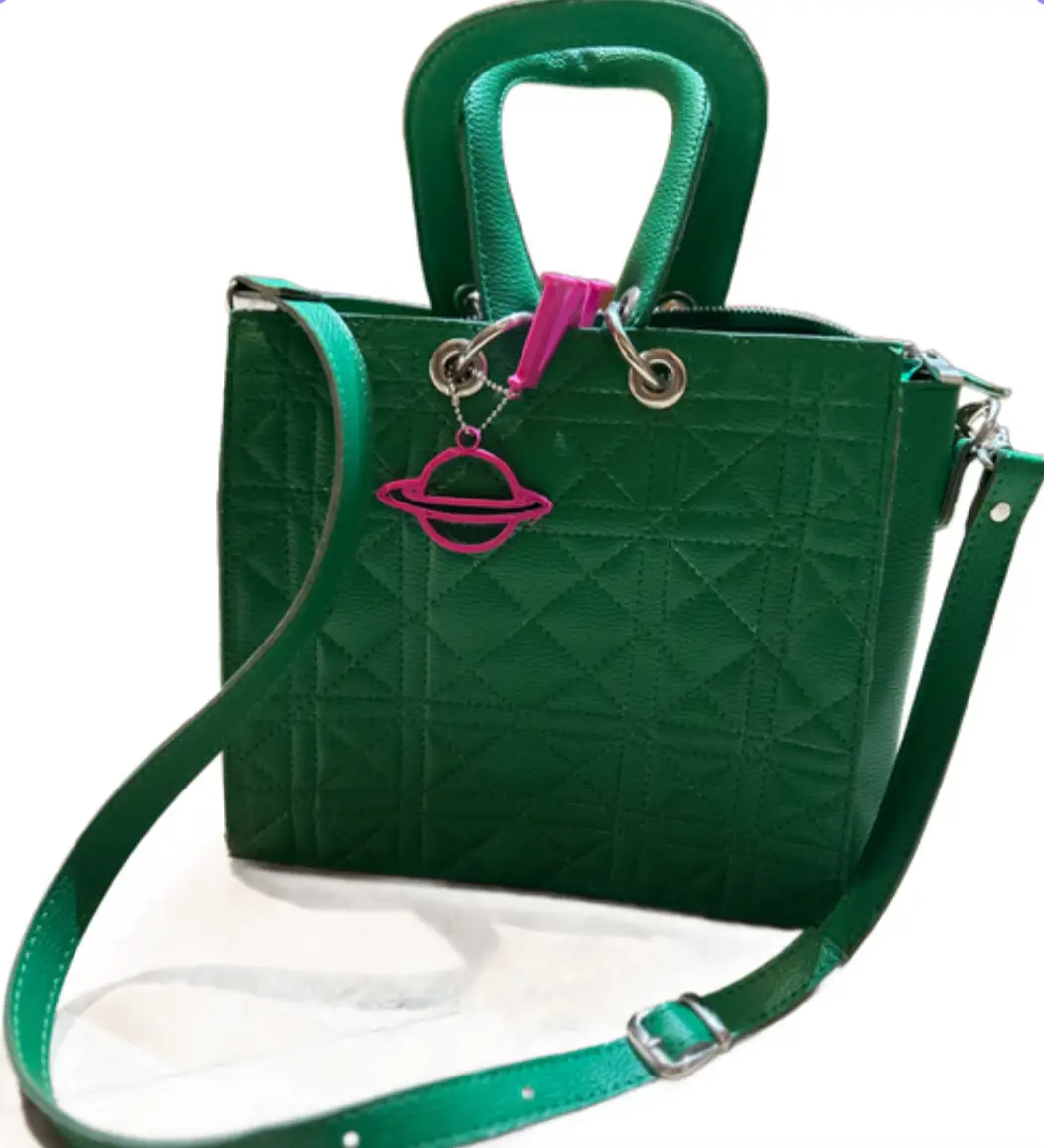 Cartera verde con diseño acolchado, manija superior y correa ajustable. Incluye un dije rosa con forma de planeta. Ideal para un look moderno y casual.